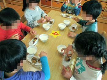 自分たちで作った紙容器で、おやつの大学芋を食べる４歳児たち