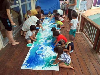 大きな模造紙に水色の絵の具を手に付けて絵を描く園児たち