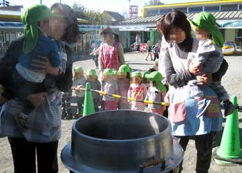 保育士に抱き上げられぶり大根を料理する大釜をのぞき込む１歳児